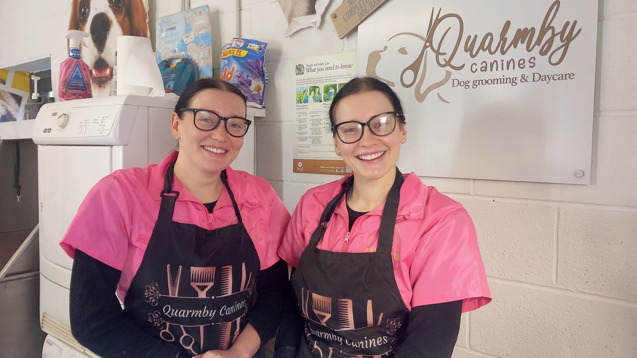 The Quarmby Canines salon team in their pink grooming uniforms beside the salon sign